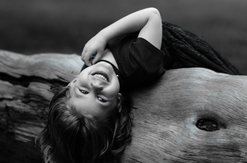 Black and white portrait of a girl wearing a flowy black dress laying on a fallen tree with a grey background, Lyssa Benavidez Photography Elkhorn, NE Lyssab.com Family photography. 