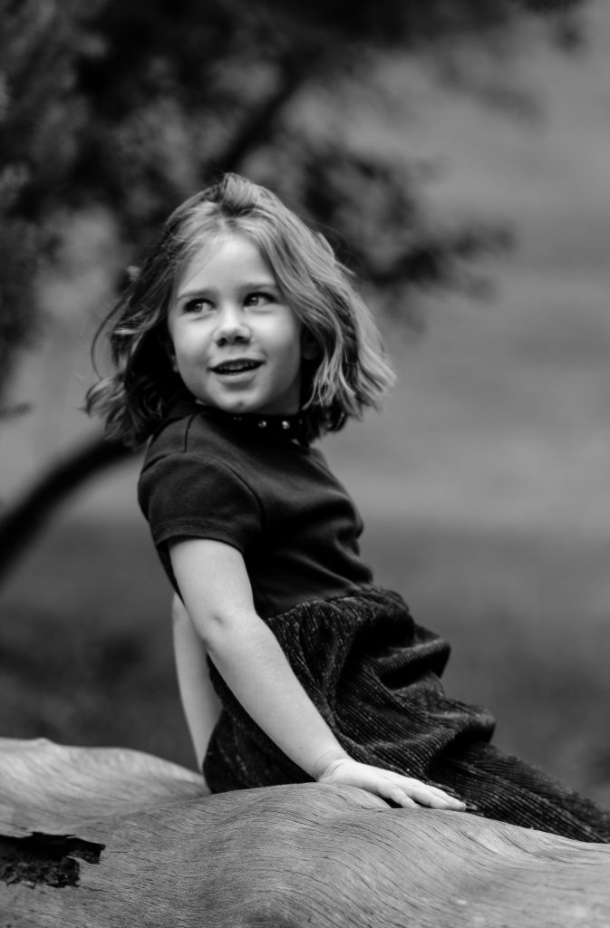 Black and white portrait of a girl wearing a flowy black dress sitting on a fallen tree with trees in the background, Lyssa Benavidez Photography Elkhorn, NE Lyssab.com Family photography. 