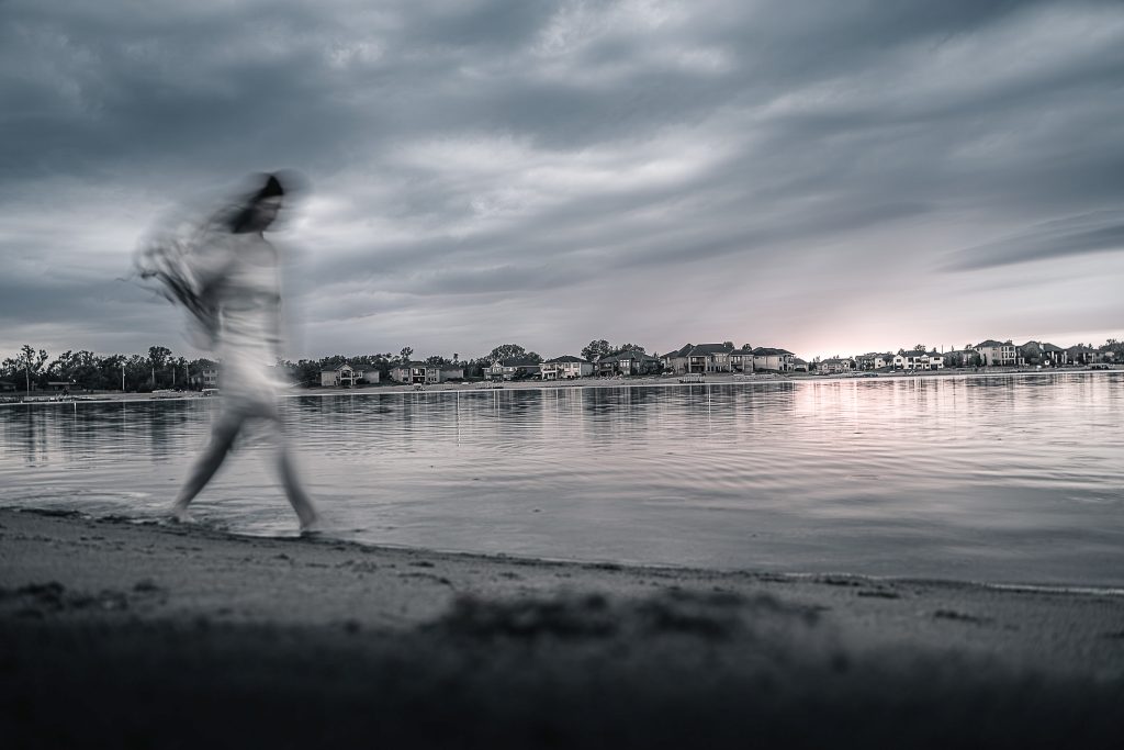 Low contrast image of a blurry figure walking on a beach with houses in the background