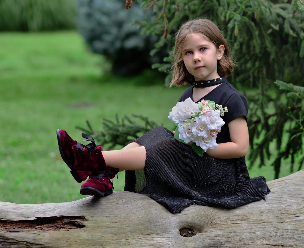 Portrait of a girl wearing a flowy black dress with deep red boots, holding a bouquet of white and pink flowers, sitting on a fallen tree with trees in the background, Lyssa Benavidez Photography Elkhorn, NE Lyssab.com Family photography. 
