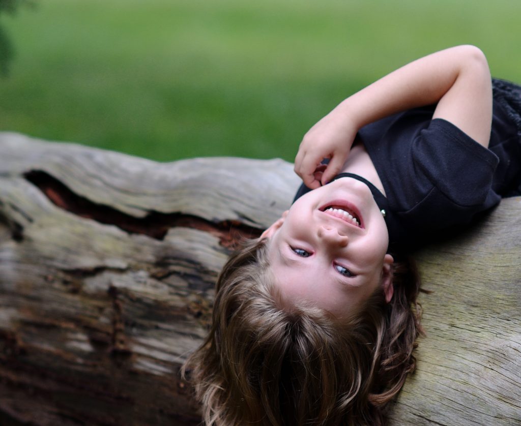 Portrait of a girl wearing a flowy black dress laying on a fallen tree with trees in the background, Lyssa Benavidez Photography Elkhorn, NE Lyssab.com Family photography. 