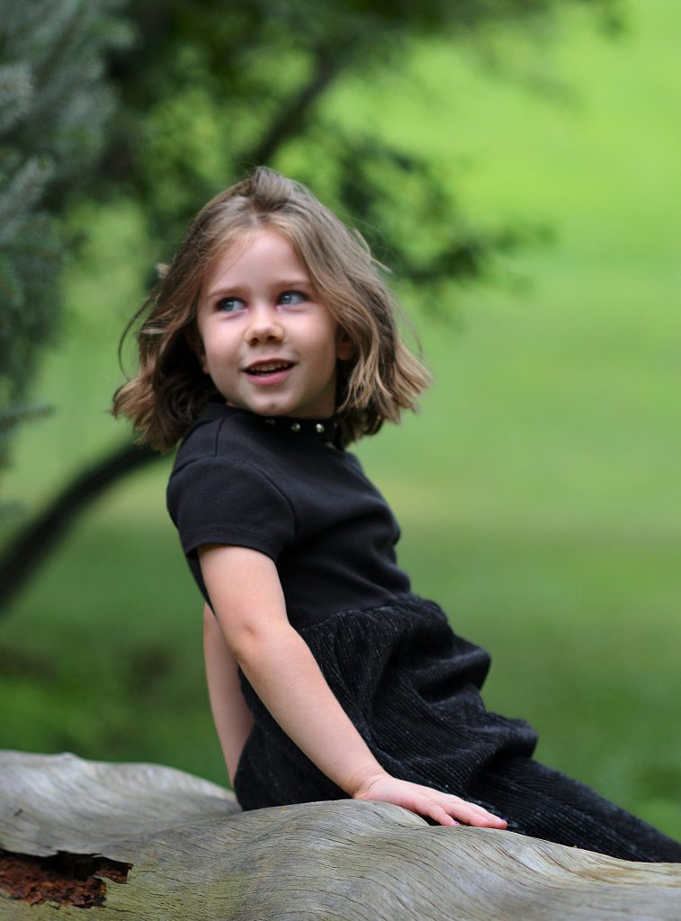 Portrait of a girl wearing a flowy black dress sitting on a fallen tree with trees in the background, Lyssa Benavidez Photography Elkhorn, NE Lyssab.com Family photography. 