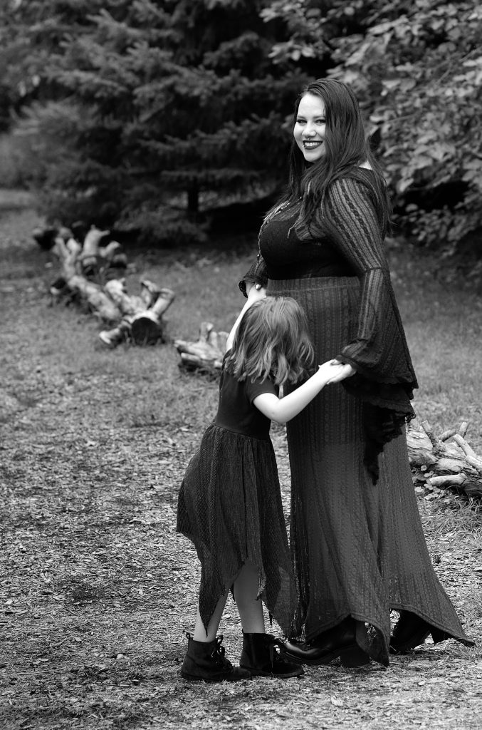 Black and white outdoor family portrait of a mom and her daughter dancing on a tree lined walking path at OPPD abortorium in Omaha NE. The mom is wearing a black long sleeved top with a dark skirt and black boots. The girl is wearing a flowy black dress with dark boots.  Lyssa Benavidez Photography Elkhorn, NE Lyssab.com Family photography. 