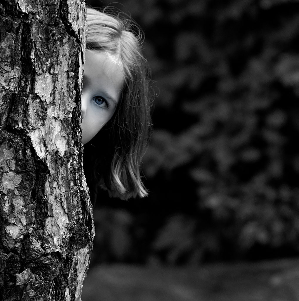 Black & white close up portrait of a girl peeking over a tree trunk with bushes in the background.  Lyssa Benavidez Photography Elkhorn, NE Lyssab.com Family photography. 