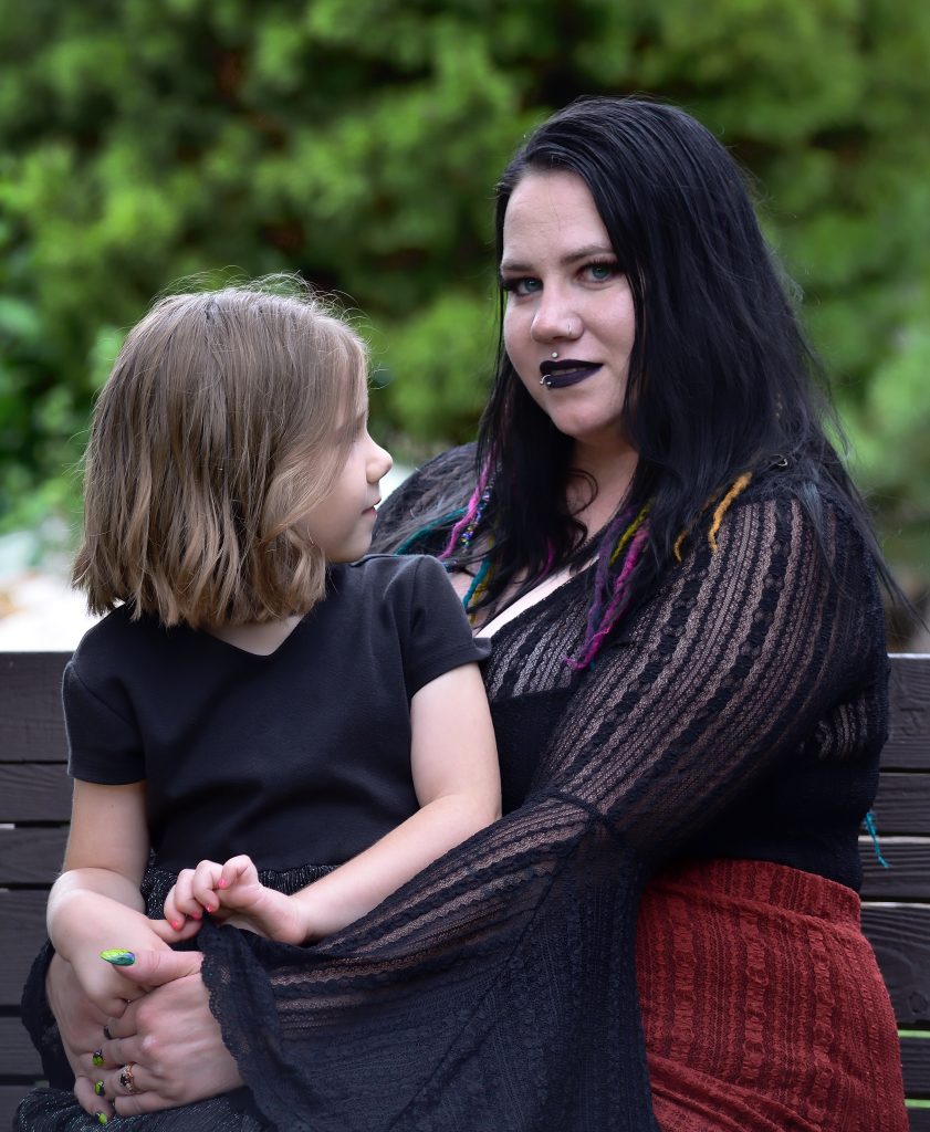 Outdoor family portrait of a mom and her daughter sitting together. The mom is wearing a black long sleeved top with a red skirt and black boots. The girl is wearing a flowy black dress with deep red boots.  Lyssa Benavidez Photography Elkhorn, NE Lyssab.com Family photography. 