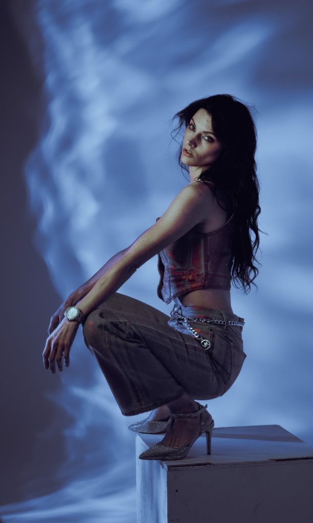 Creative light photo of a woman sitting on a white box wearing blue and red colored, shiny clothing with a blue and white light background. Lyssa Benavidez Photography Elkhorn, NE Lyssab.com studio photography. 