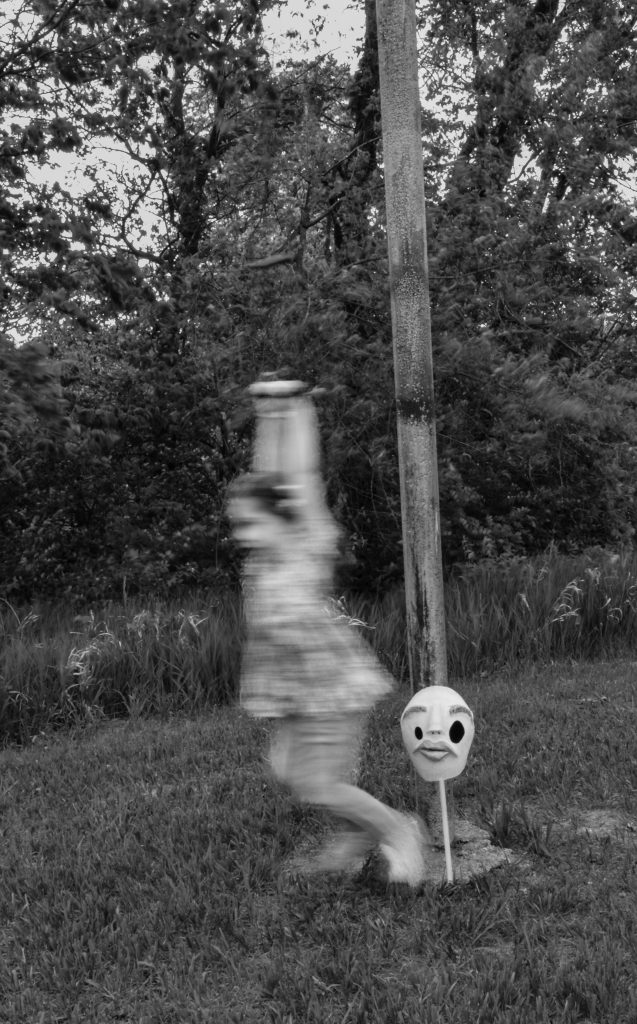 Surrealist portrait of a little girl swinging on an old abandoned swing. She's blurry but everything else around her is crisp. There's a creepy humanoid mask on the ground next to her. Lyssa Benavidez Photography Elkhorn, NE Lyssab.com surrealist photography 