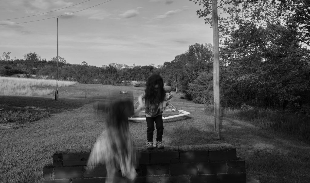 Ralph Eugune Meatyard style creative black and white portrait of two little kids jumping off a platform with trees and a merry-go-round in the background in Plattsmouth NE. The girls are blurry but everything else is crisp. Lyssa Benavidez Photography Elkhorn, NE Lyssab.com Creative/Fine art photography surrealist photography.