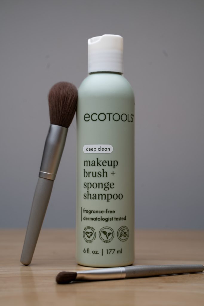 Product photo for Ecotools makeup brush + sponge shampoo with the product front and center surrounded by two grey and brown makeup brushes against a clean grey background sitting on top of a light brown table. Lyssa Benavidez Photography Elkhorn, NE Lyssab.com Product photography.