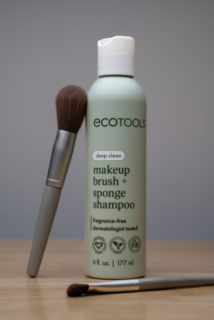Product photo for Ecotools makeup brush + sponge shampoo with the product front and center surrounded by two grey and brown makeup brushes against a clean grey background sitting on top of a light brown table. Lyssa Benavidez Photography Elkhorn, NE Lyssab.com Product photography.