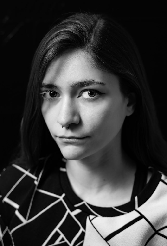 Black & white portrait of a woman with long hair wearing a black and white shirt looking at the camera standing in front of a black background with dramatic lighting. Lyssa Benavidez Photography Elkhorn, NE Lyssab.com studio fine art photography