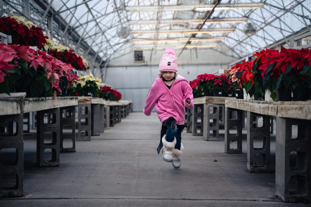 Portrait of a girl running down an aisle with plants in the background. Lyssa Benavidez Photography Elkhorn, NE Lyssab.com Lifestyle family photography