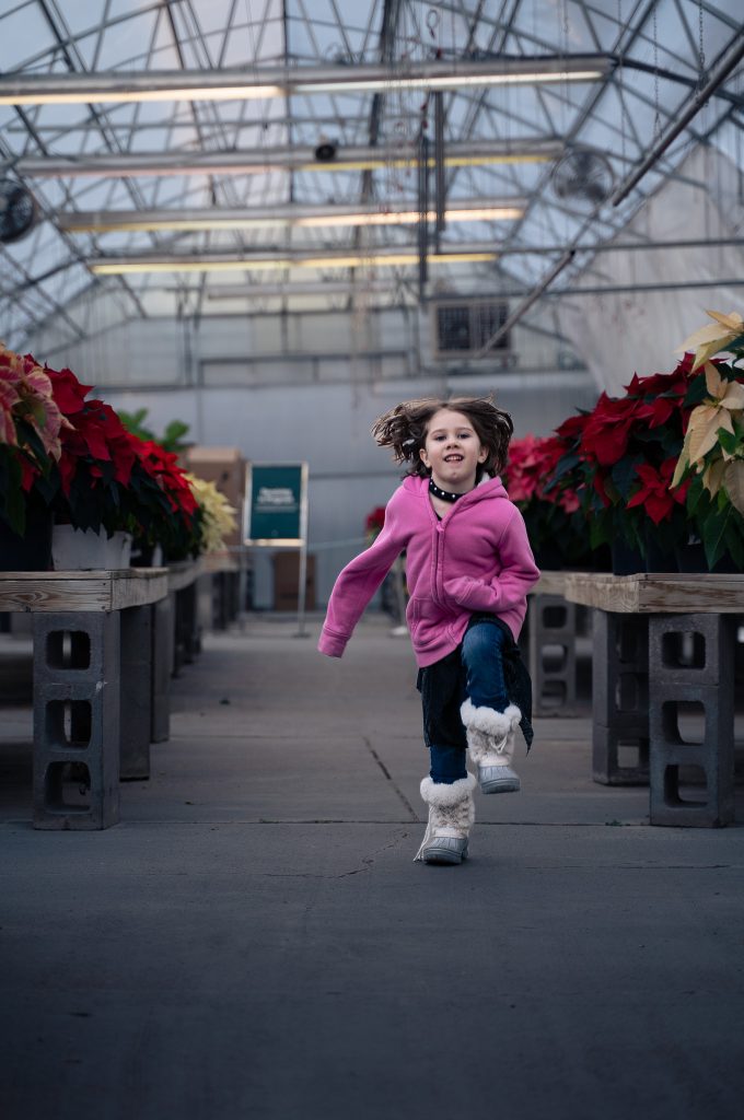Portrait of a girl running down an aisle with plants in the background. Lyssa Benavidez Photography Elkhorn, NE Lyssab.com Lifestyle family photography