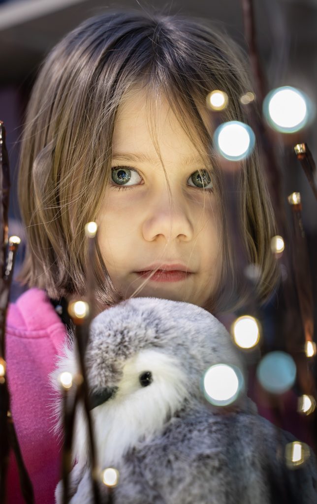 Portrait of a little girl wearing a pink shirt holding a stuffed animal with creative light spots in front of her. Lyssa Benavidez Photography Elkhorn, NE Lyssab.com Lifestyle family photography