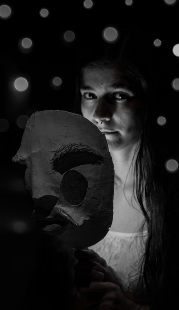 Surrealist black and white portrait of a woman showing her face behind a creepy humanoid mask with white orbs floating around her against a black background.  Lyssa Benavidez Photography Elkhorn, NE Lyssab.com Fine Art Photography surrealist photography