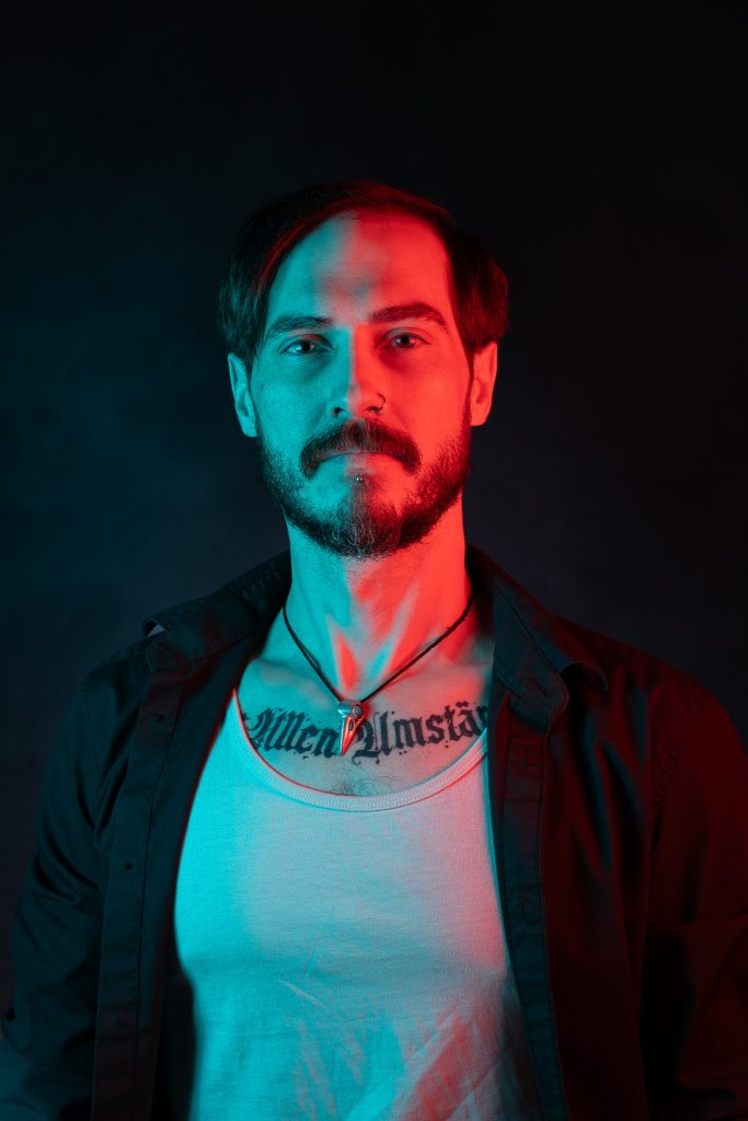 Creative light portrait of a man wearing a black and white shirt, with red and blue creative lighting standing in front of a dark blue background. Lyssa Benavidez Photography Elkhorn, NE studio photography. 