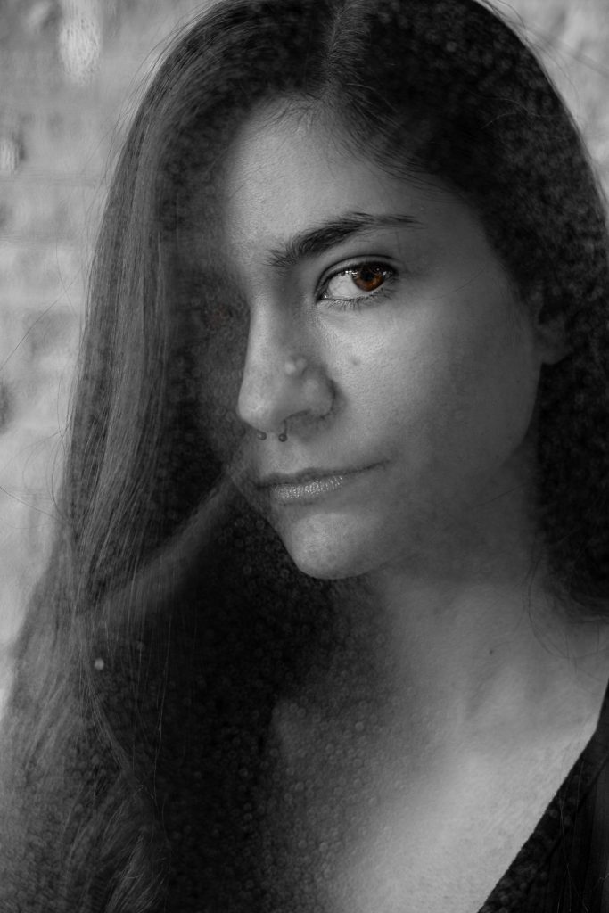 Black & white portrait of a woman with long hair wearing a black shirt looking at the camera standing in front of a white background with dramatic lighting. Lyssa Benavidez Photography Elkhorn, NE Lyssab.com studio fine art photography