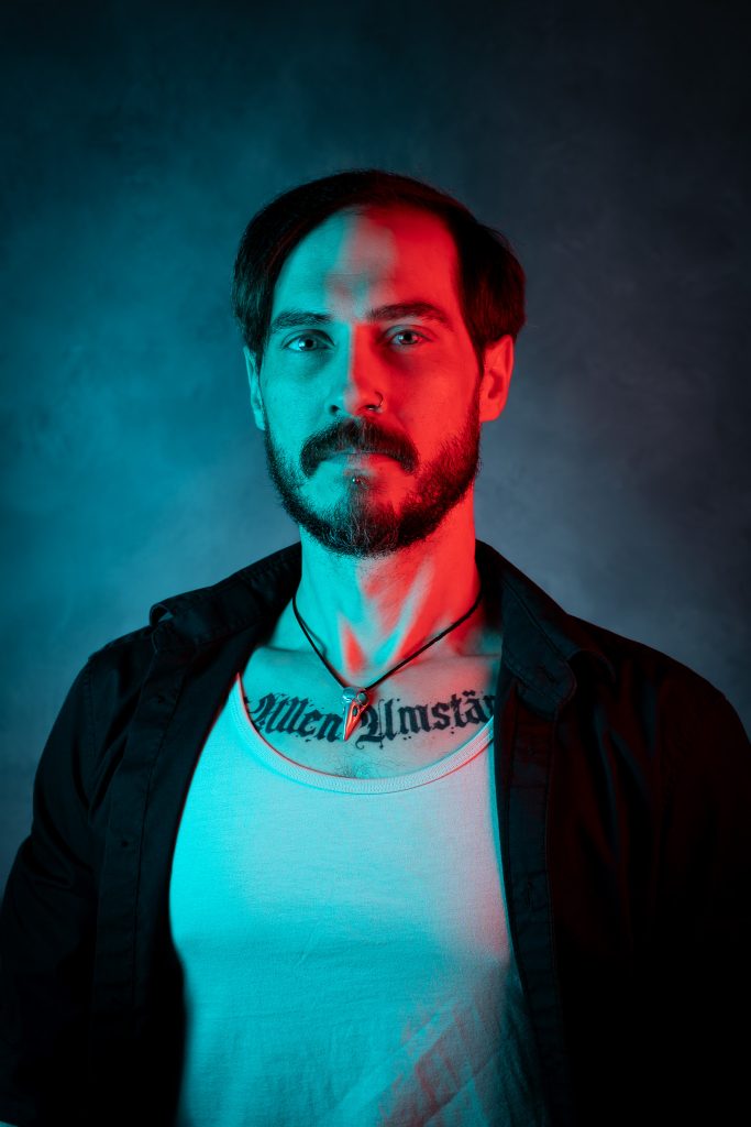 Creative light portrait of a man wearing a black and white shirt, with red and blue creative lighting standing in front of a dark blue background. Lyssa Benavidez Photography Elkhorn, NE studio photography. 