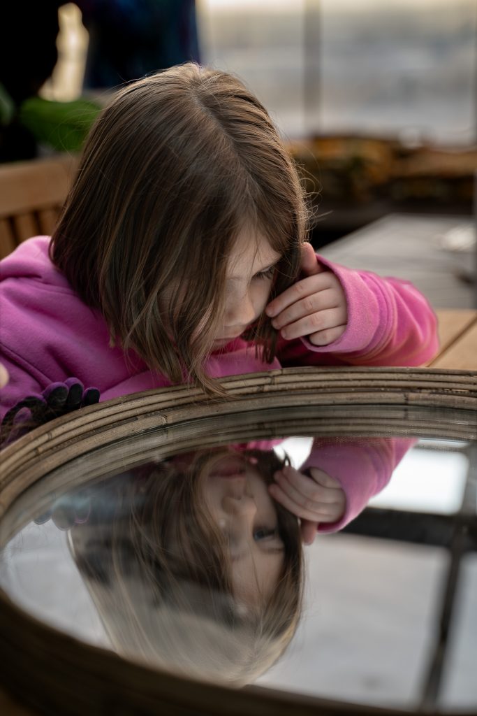 Portrait of a little girl looking into a mirror and wearing a pink shirt. Lyssa Benavidez Photography Elkhorn, NE Lyssab.com Lifestyle family photography