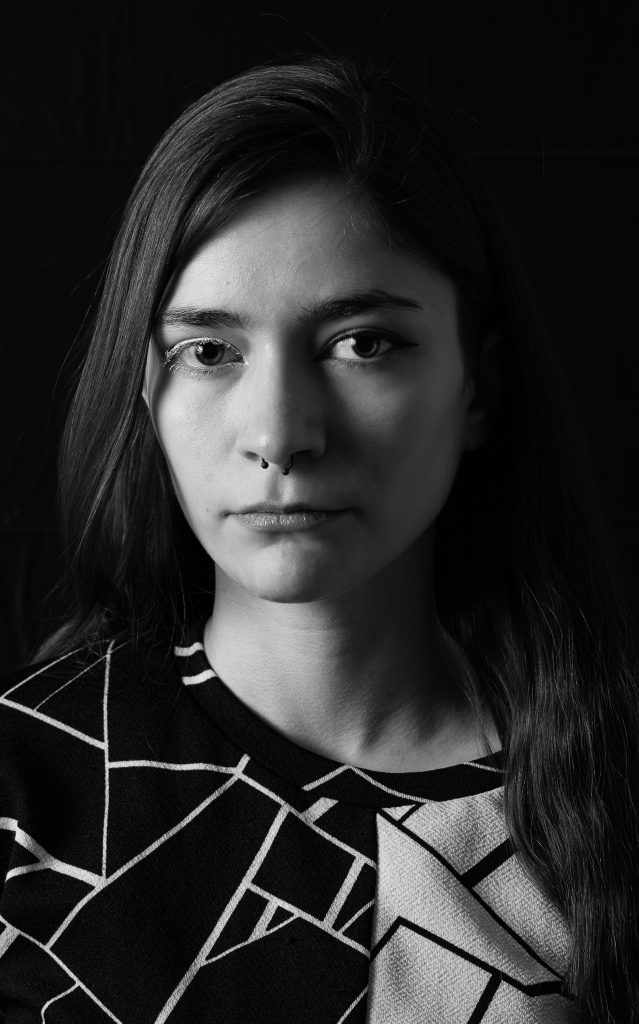 Black & white portrait of a woman with long hair wearing a black and white shirt looking at the camera standing in front of a black background with dramatic lighting. Lyssa Benavidez Photography Elkhorn, NE Lyssab.com studio fine art photography