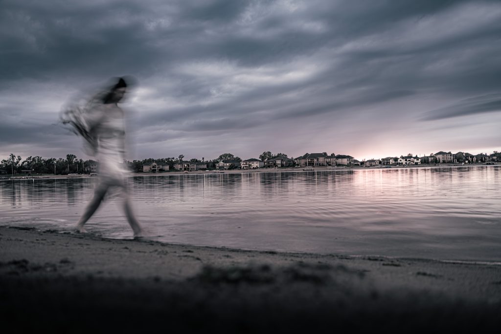 Surrealist portrait of a woman in a white dress walking along a beach. The woman has intentional motion blur and everything else is crisp. Lyssa Benavidez Photography Elkhorn, NE Lyssab.com Surrealist photography