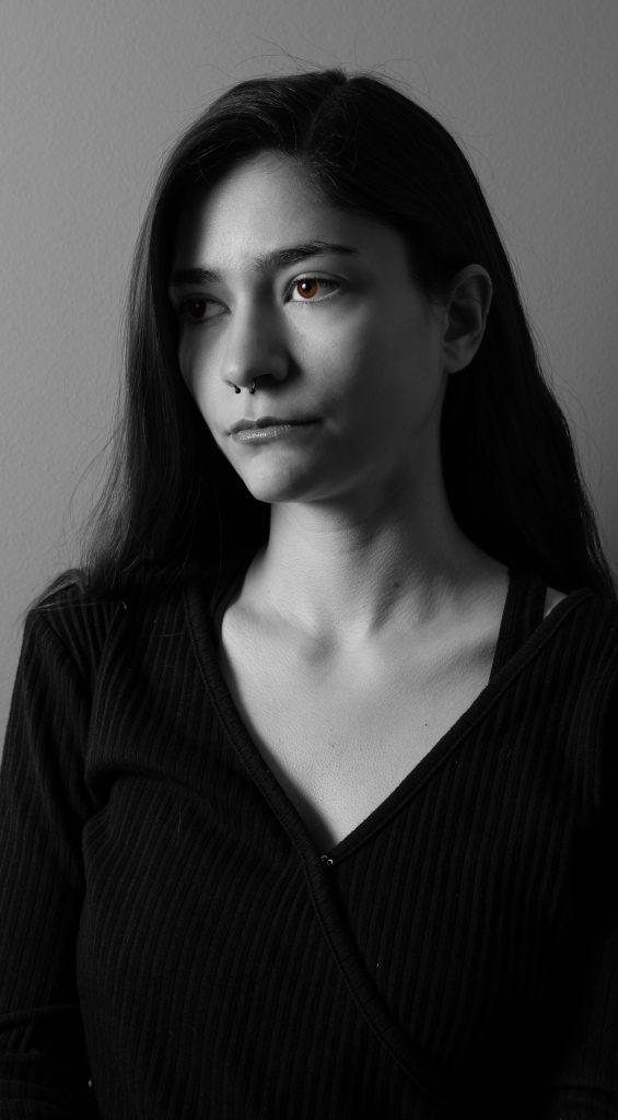 Black and white portrait of a woman with long hair wearing a black shirt looking off into the distance standing in front of a grey background with dramatic lighting. Lyssa Benavidez Photography Elkhorn, NE Lyssab.com studio fine art photography